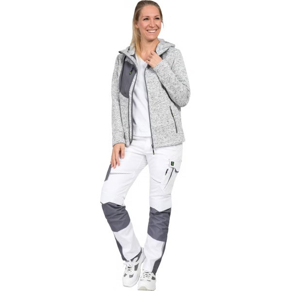Frau in einer grauen Strickfleecejacke mit Kapuze und einer weiß-grauen Arbeitshose mit Knieverstärkungen und Taschen.