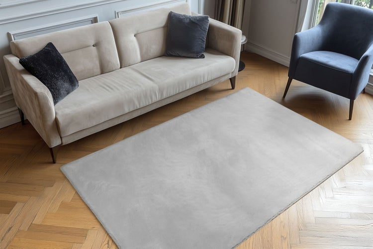 Ein rechteckiger Teppich vor einem Sofa und einem Sessel in einem Wohnzimmer mit Fischgrätparkett.