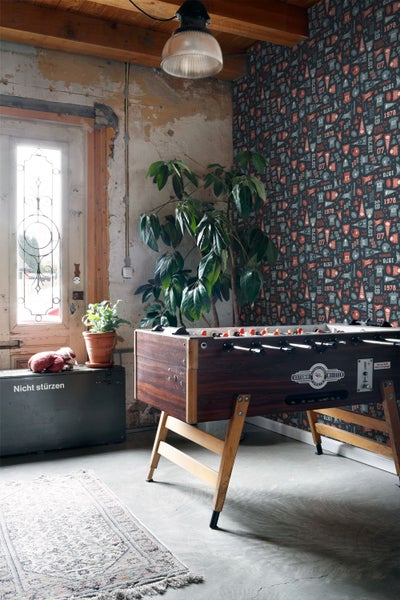 Innenraum mit Tischfußball, Pflanze, dekorativer Tapete und altem Koffer