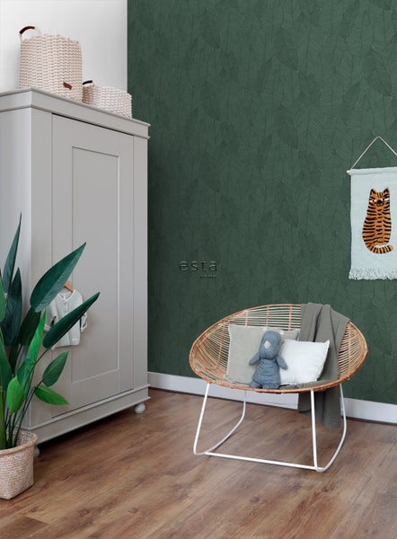 Ein Kinderzimmer mit einem grauen Kleiderschrank, einem Rattansessel und einer grünen Tapete mit Blattmuster