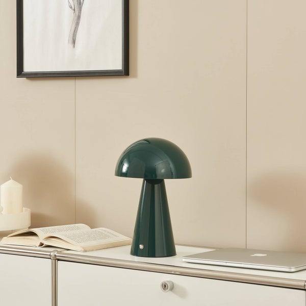 Moderne, pilzförmige Tischleuchte in Dunkelgrün auf weißem Sideboard neben Buch und Laptop in hellem, aufgeräumtem Raum.