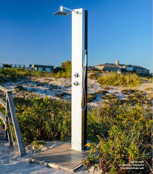 Solardusche Tobago Solar mit weißer Sicherheitsglasfront, Regenduschkopf und Handbrause in einer Dünenlandschaft.