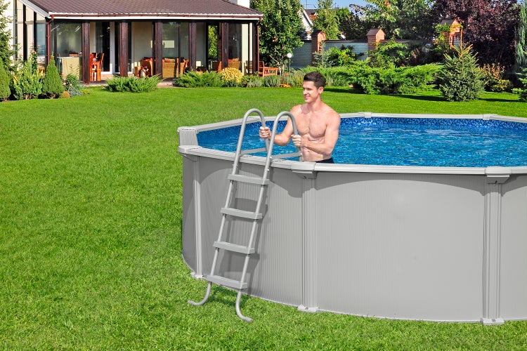 Grauer runder Aufstellpool mit blauer Innenfolie und Poolleiter auf einer Rasenfläche im Garten, ein Mann steht im Wasser.