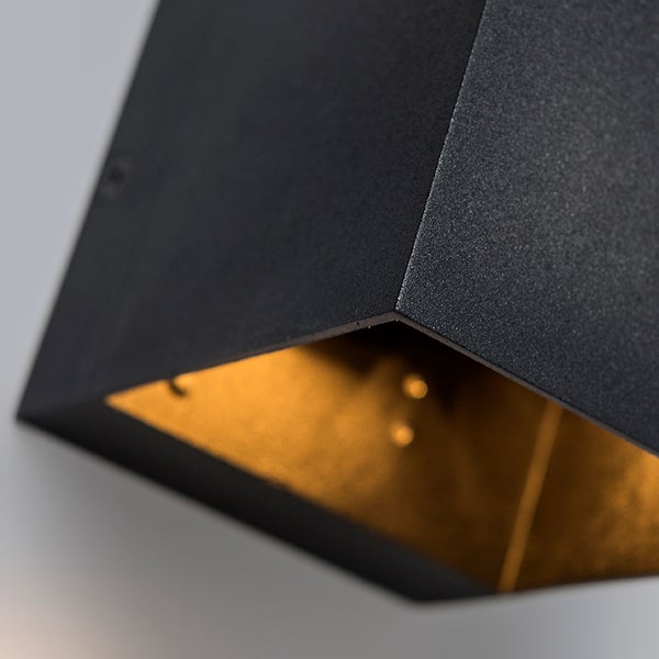 Detailansicht einer eckigen Wandleuchte mit strukturierter matt-schwarzer Oberfläche und goldfarben beschichteter Innenseite.