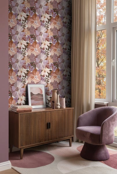 Wohnzimmer mit floraler Tapete in Mauve und Orange, einem hölzernen Sideboard, einem lila Samtsessel und beigefarbenen Vorhängen am Fenster.