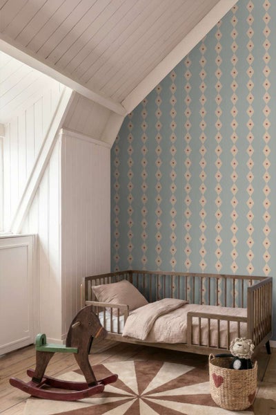 Kinderzimmer mit Tapete mit Rautenmuster, Holzgitterbett, Schaukelpferd und geflochtenem Korb auf einem runden Teppich.