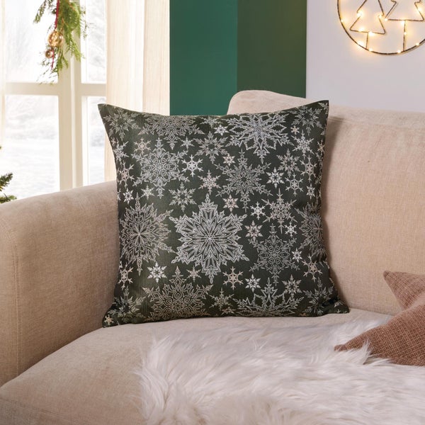 Quadratisches Dekokissen mit weihnachtlichem Schneeflockenmuster auf einem hellen Sofa in einem geschmückten Wohnzimmer.