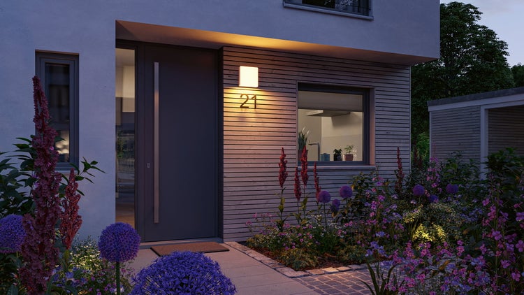 Quadratische Außenwandleuchte über der Hausnummer einundzwanzig an einem Hauseingang mit Holzfassade und bepflanztem Gartenbeet.