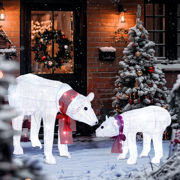 Zwei beleuchtete Eisbären-Weihnachtsfiguren mit roten Schals in einer verschneiten Außenszene mit Weihnachtsbaum und Türkranz vor einem Backsteinhaus.
