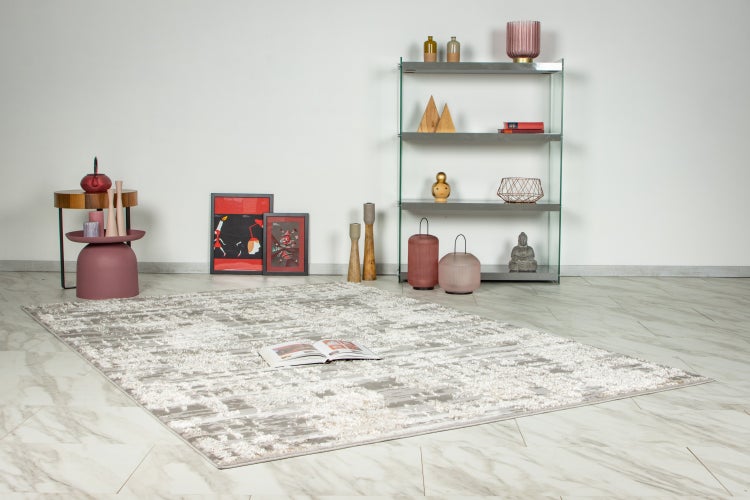 Ein moderner Hochflor Teppich mit geometrischem Muster liegt auf einem hellen Marmorboden in einem Raum mit Regal und Beistelltisch.