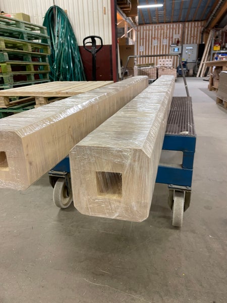 Zwei in Folie verpackte quadratische Holzbalken mit mittiger Aussparung in einem Lager.