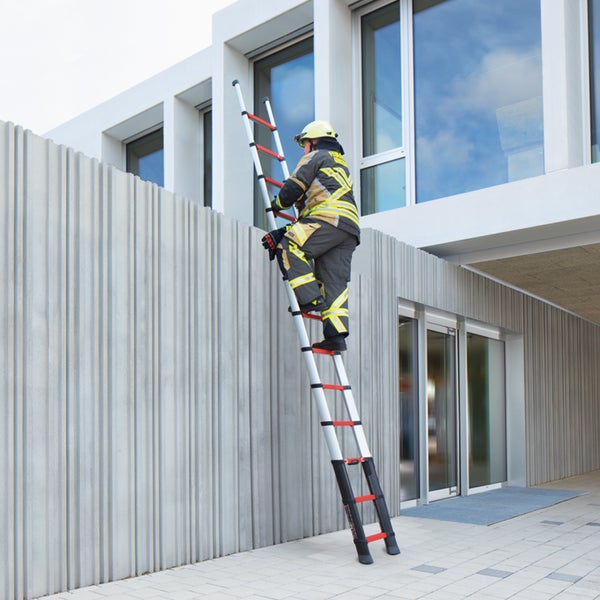 Feuerwehrmann auf einer ausgezogenen Teleskopleiter an einem modernen Gebäude mit strukturierter Betonfassade.