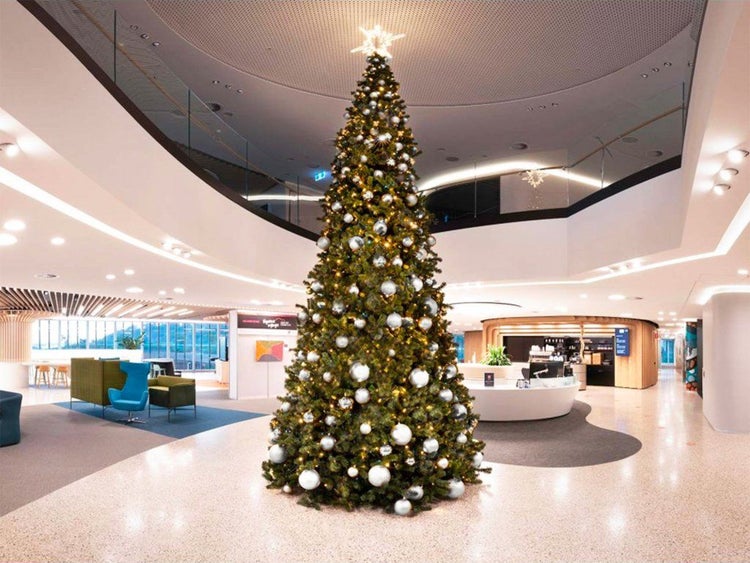 Großer geschmückter Weihnachtsbaum mit silbernen Kugeln und Lichterkette in einem modernen, geräumigen Foyer eines Bürogebäudes.