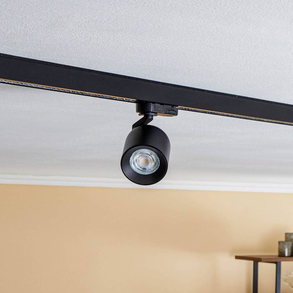 Schwarzer Schienenstrahler an einer schwarzen Stromschiene an der Decke montiert.