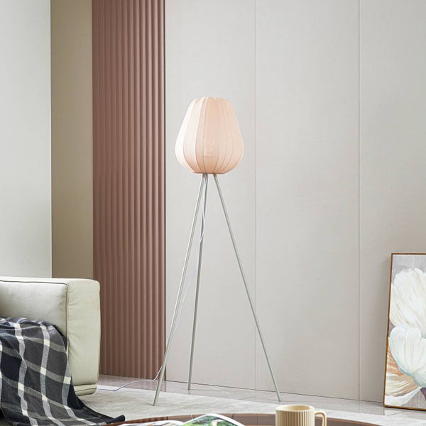 Moderne Dreibein-Stehleuchte mit plissiertem Stoffschirm in einem hellen Wohnzimmer neben einem Sofa mit karierter Decke.