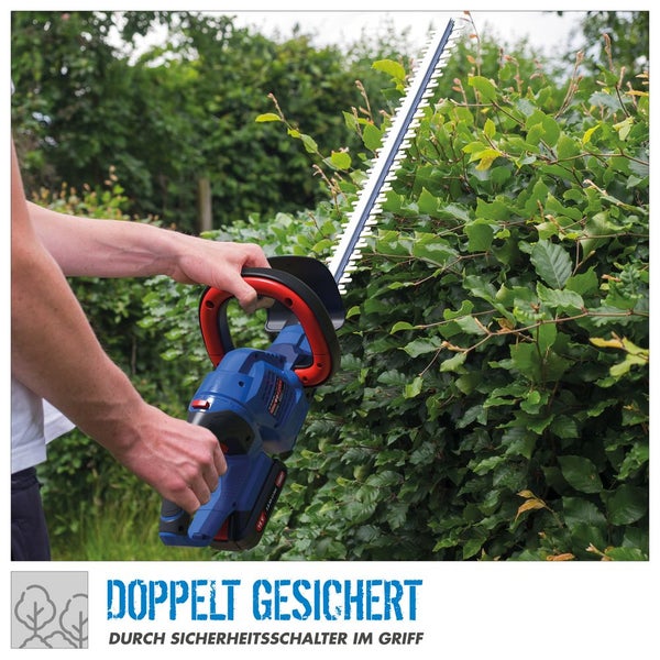 Person schneidet eine Hecke mit einer Akku-Heckenschere. Das Werkzeug verfügt über einen doppelten Sicherheitsschalter am Handgriff.