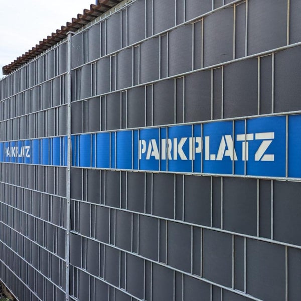 Drahtzaun mit Sichtschutz und der Aufschrift Parkplatz