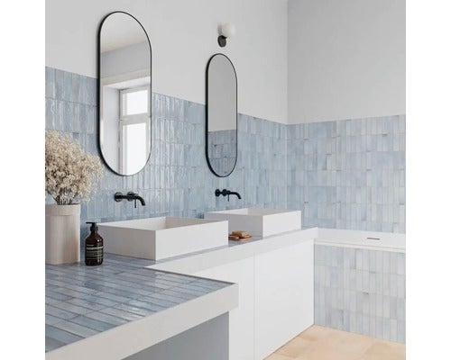 Modernes Badezimmer mit Doppelwaschbecken, ovalen Spiegeln, Wandarmaturen sowie gefliesten Wänden und Waschtisch. Hell und organisiert.