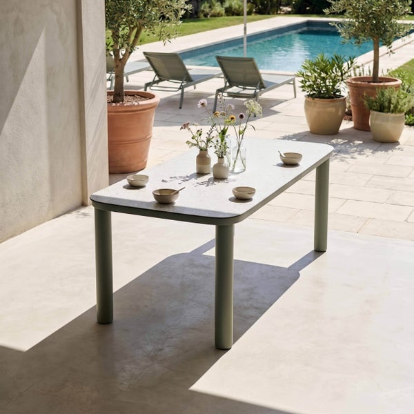 Moderner rechteckiger Gartentisch auf einer hellen Terrasse neben einem Pool, dekoriert mit Vasen, umgeben von Olivenbäumen und Liegestühlen.