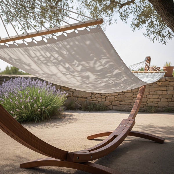 Hängematte mit geschwungenem Holzgestell und Spreizstab aus Holz in einem Garten mit Lavendelstrauch und Steinmauer.