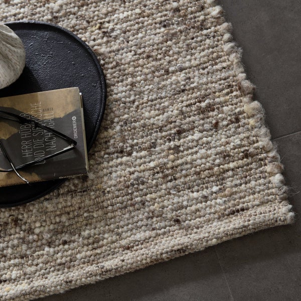 Nahaufnahme eines beigen Teppichs mit Buch, Brille und Dekoration auf einem Tablett