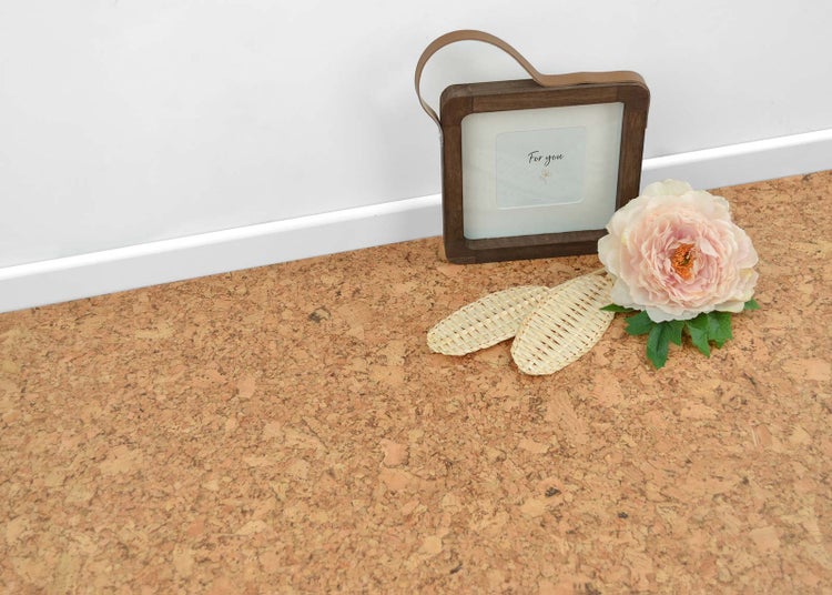 Korkboden mit natürlicher Textur, weißer Fußleiste, dekorativem Bilderrahmen aus Holz und künstlicher Blume in einem hellen Raum.