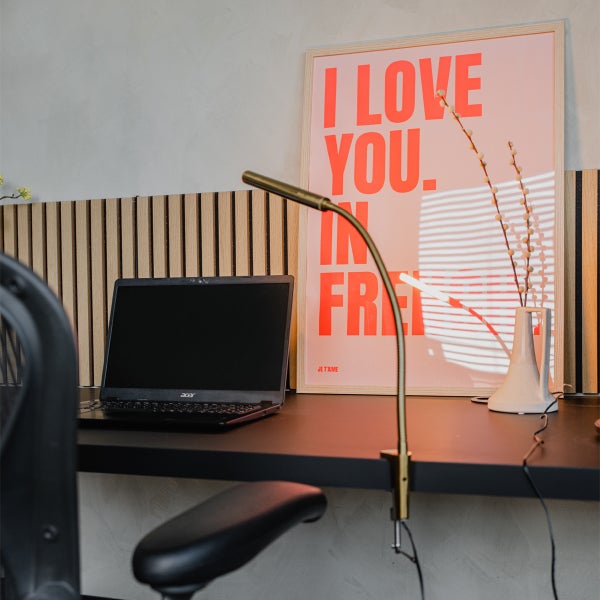 Schreibtisch mit Laptop, Klemmleuchte, Bild mit Aufschrift und Dekoration