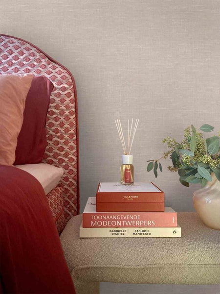 Strukturierte Vliestapete mit Textiloptik in einem hellen Schlafzimmer hinter einem Bett und Büchern mit einem Raumduft.