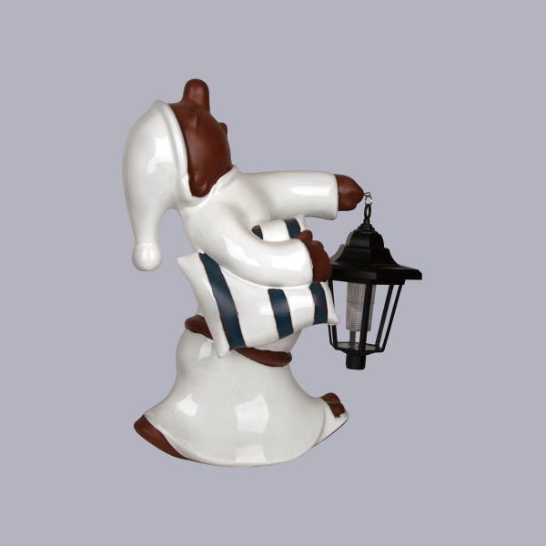 Gartenfigur Bär in weißem Nachthemd mit Solarlaterne und gestreiftem Kissen.