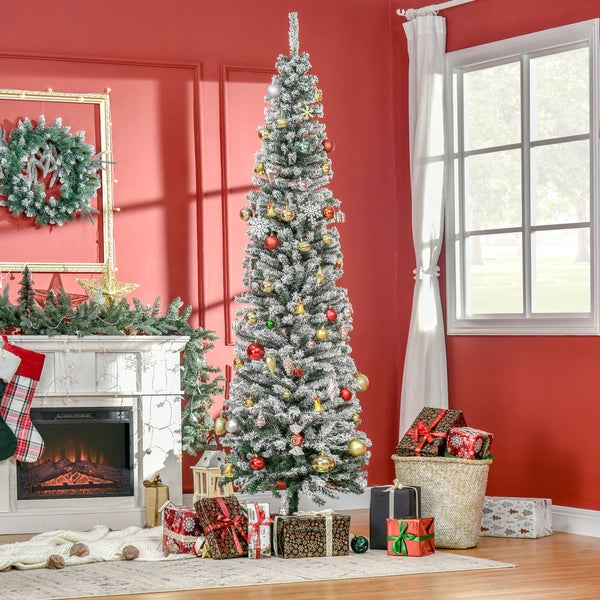 Festlich dekorierter Raum mit schmalem, beschneitem künstlichem Weihnachtsbaum, Kamin mit Girlande und Geschenken vor roter Wand.