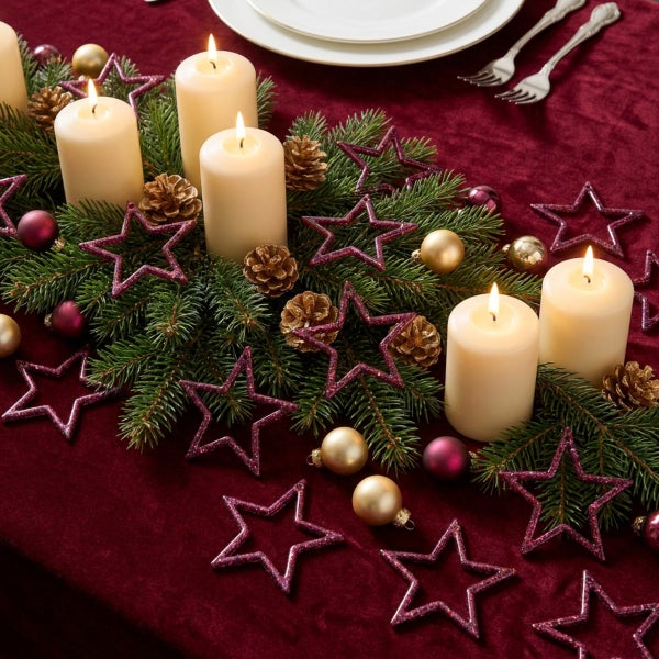 Weihnachtliche Tischdekoration mit Tannenzweigen, Stumpenkerzen, glitzernden Sternen, Weihnachtskugeln und Tannenzapfen auf einem Tisch.