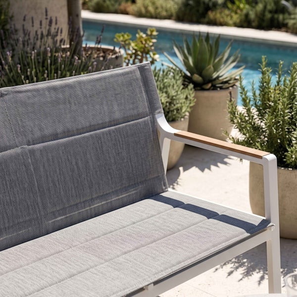 Gartenbank mit weißem Aluminiumgestell, grauer Textilbespannung und Holzarmlehnen im Außenbereich an einem Pool.