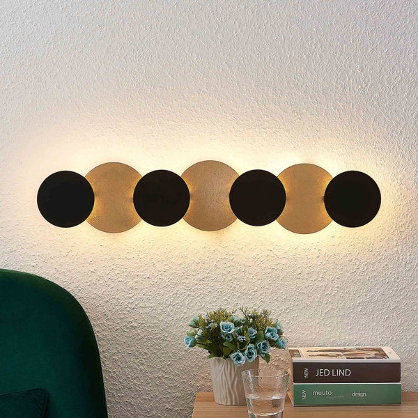 Moderne LED Wandleuchte mit sieben überlappenden, kreisförmigen Metallscheiben in Schwarz und Gold für indirekte Beleuchtung.