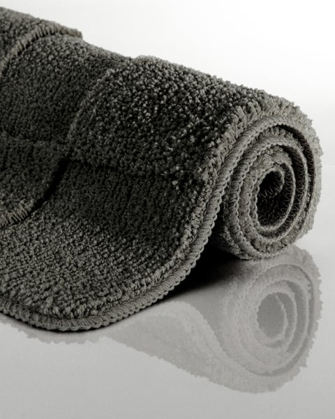 Runder dunkelgrauer Badteppich mit geometrischem Muster auf Holzfußboden neben einer weißen Badewanne.