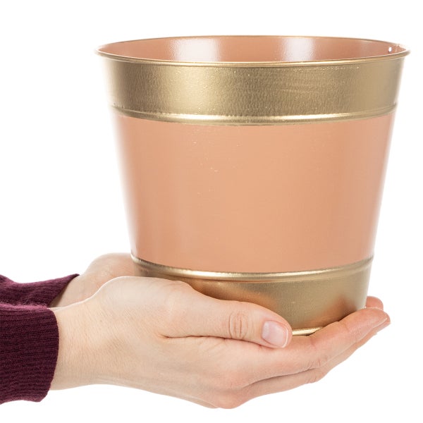 Übertopf aus Metall in Roségold und Gold, gehalten von zwei Händen zur Demonstration der Größe.