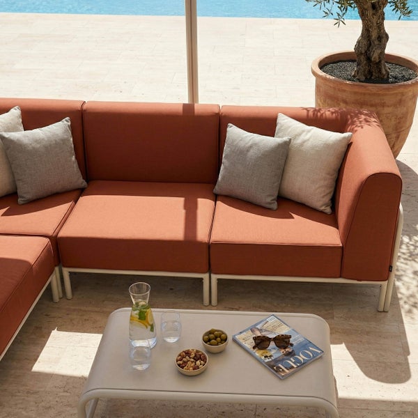 Moderner, heller Outdoor-Loungebereich mit modularem Sofa in Terracotta, hellgrauen Kissen und Loungetisch auf einer weitläufigen Steinterrasse.
