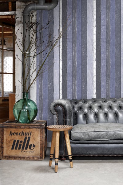 Innenraum mit Chesterfield-Sofa, Holzkiste, Hocker und dekorativer Tapete mit Holzplanken-Optik.