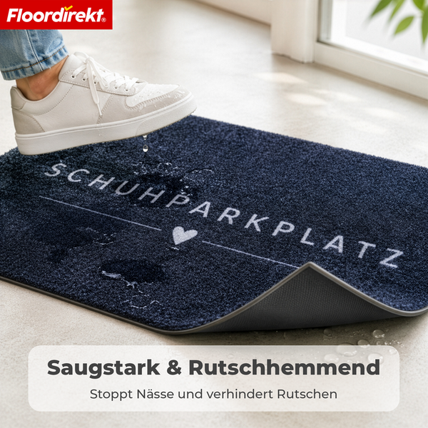 Saugstarke, rutschhemmende Schmutzfangmatte mit Aufschrift Schuhparkplatz, ein Schuh tritt auf die nasse Oberfläche. Floordirekt Logo.