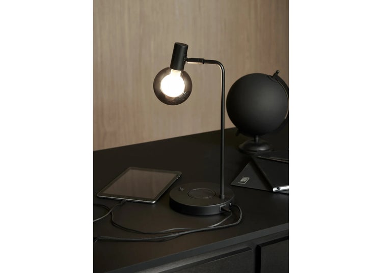 Moderne Schreibtischlampe mit Kugelglaskopf und integrierter Ladestation auf einem dunklen Schreibtisch mit Globus und Notizbuch.