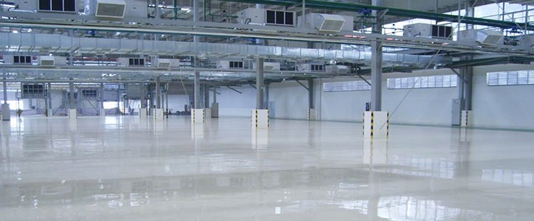 Große Industriehalle mit glänzendem, reflektierendem Boden, Lüftungssystem an der Decke und Betonpfeilern mit Markierung.