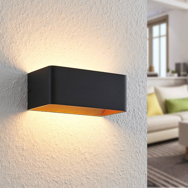 Moderne rechteckige Wandleuchte in Schwarz mit goldener Innenseite, Lichtaustritt nach oben und unten, montiert an einer weißen Wand im Wohnzimmer.
