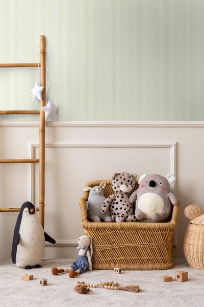 Gestreifte Tapete in einem Kinderzimmer mit einer Bambusleiter, Kuscheltieren und Rattanmöbeln.