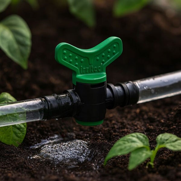Irritec Absperrventil für ein Bewässerungssystem an einem Schlauch in der Erde neben Gartenpflanzen.