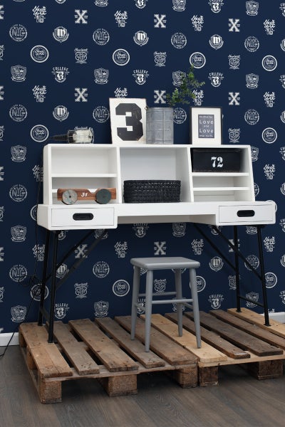 Szene mit einem Schreibtisch mit Regalen, Schubladen und Metallbeinen, einem grauen Hocker und einer Palette als Unterlage vor einer blau gemusterten Tapete.