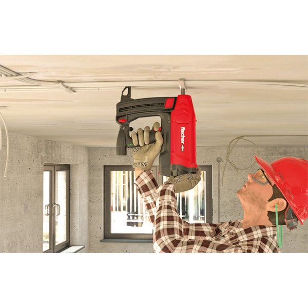 Handwerker befestigt Kabel mit einem Bolzensetzgerät der Marke Fischer an einer Betondecke.