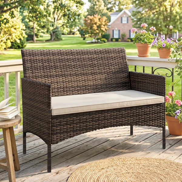Polyrattan-Gartenbank mit hellem Sitzkissen auf einer Holzterrasse in einem hellen, organisierten Garten.