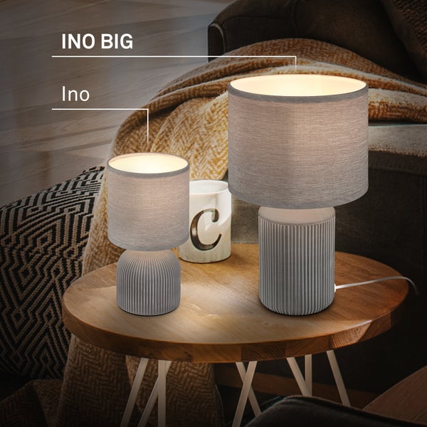 Zwei Tischleuchten Ino und Ino Big mit geriffeltem Keramikfuß und Stoffschirm auf einem hölzernen Beistelltisch in einem Wohnzimmer.