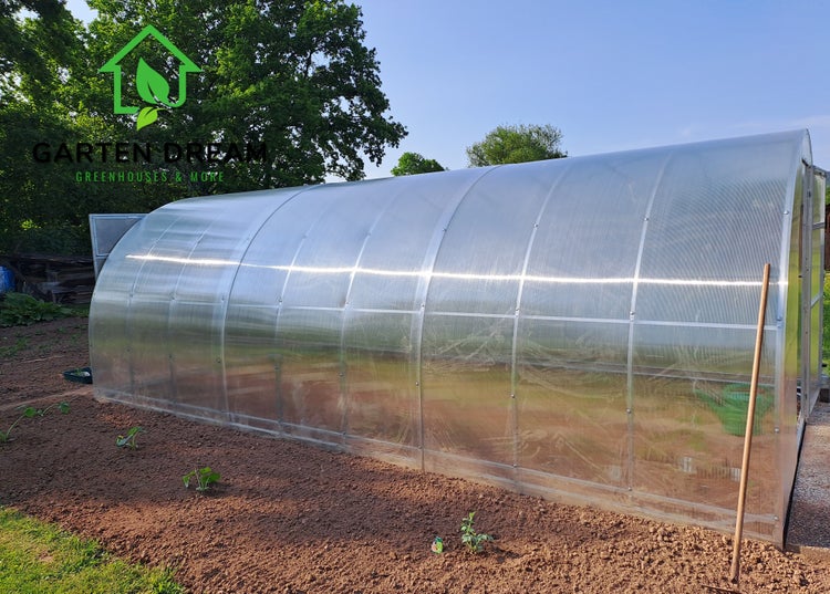 Gewächshaus im Garten mit jungen Pflanzen im Beet.