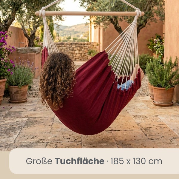 Weinroter Hängesessel mit einer Tuchfläche von 185 mal 130 Zentimetern und Holzstab, in dem eine Person im Garten sitzt.