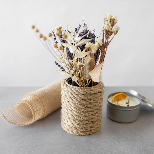 Deko-Set mit Trockenblumen in einer mit Seil umwickelten Vase, einer Juterolle und einer Duftkerze in einer Metalldose.